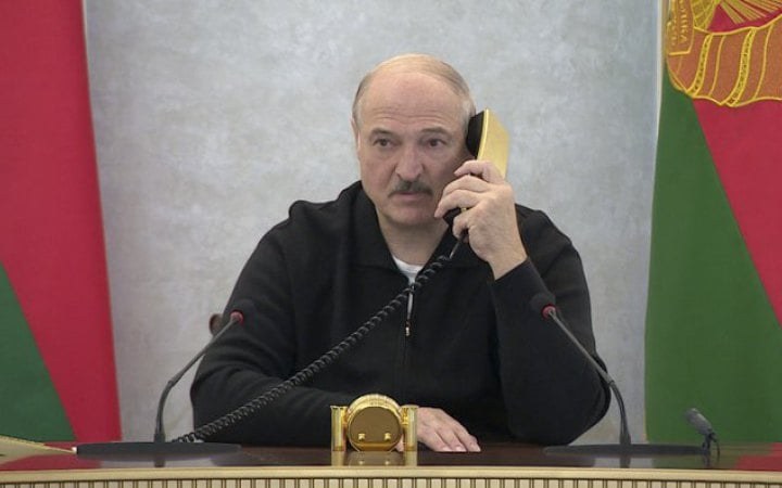 Aleksandr Lukașenko vorbește la telefon la o masă, cu steagul Belarusului în fundal.