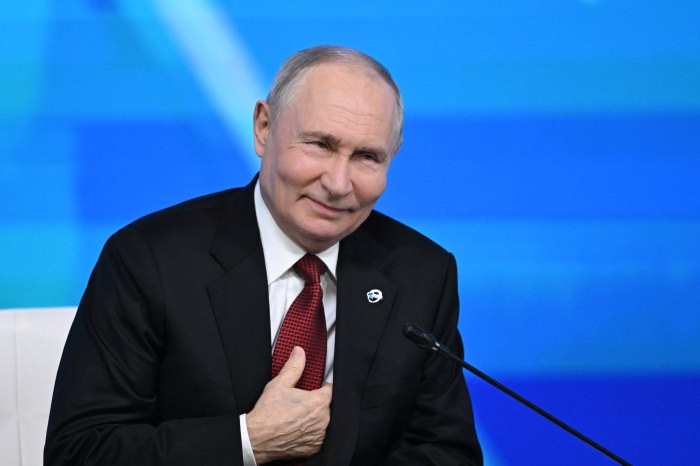 Vladimir Putin la reuniunea Clubului Valdai, așezat lângă un microfon pe un fundal albastru.