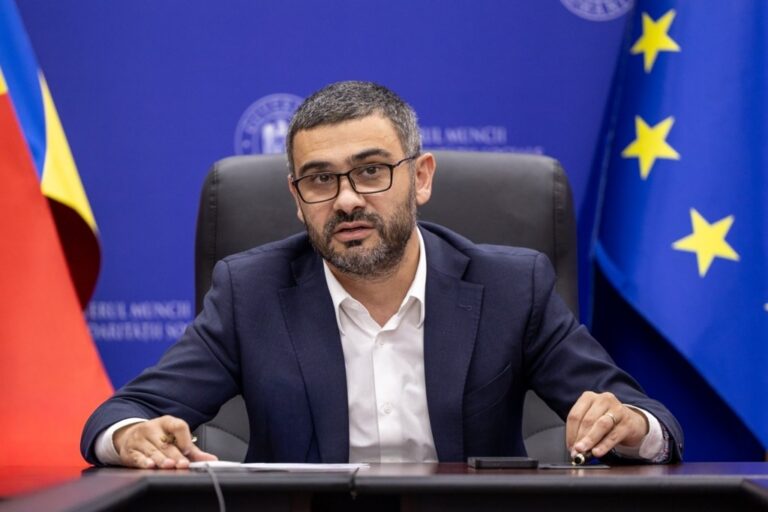 Florin Manole la o masă de lucru, între drapelele României și Uniunii Europene